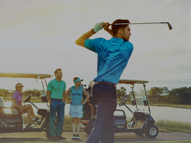 Golfer swinging on golf course with carts and foursome
